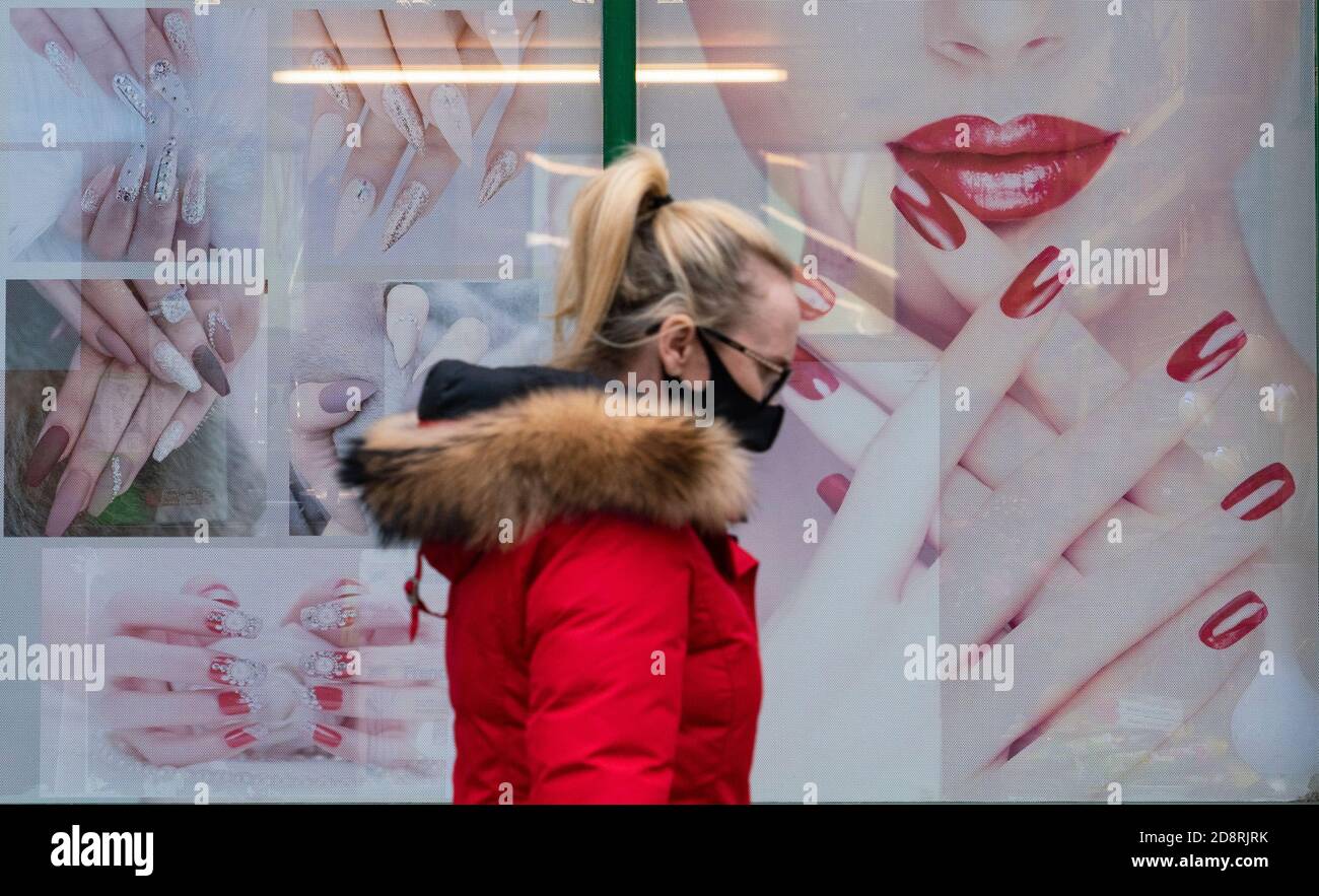 Donna che indossa facemask cammina accanto alla vetrina del bar unghie nel centro di Airdrie durante la pandemia di coronavirus, Scozia Regno Unito Foto Stock