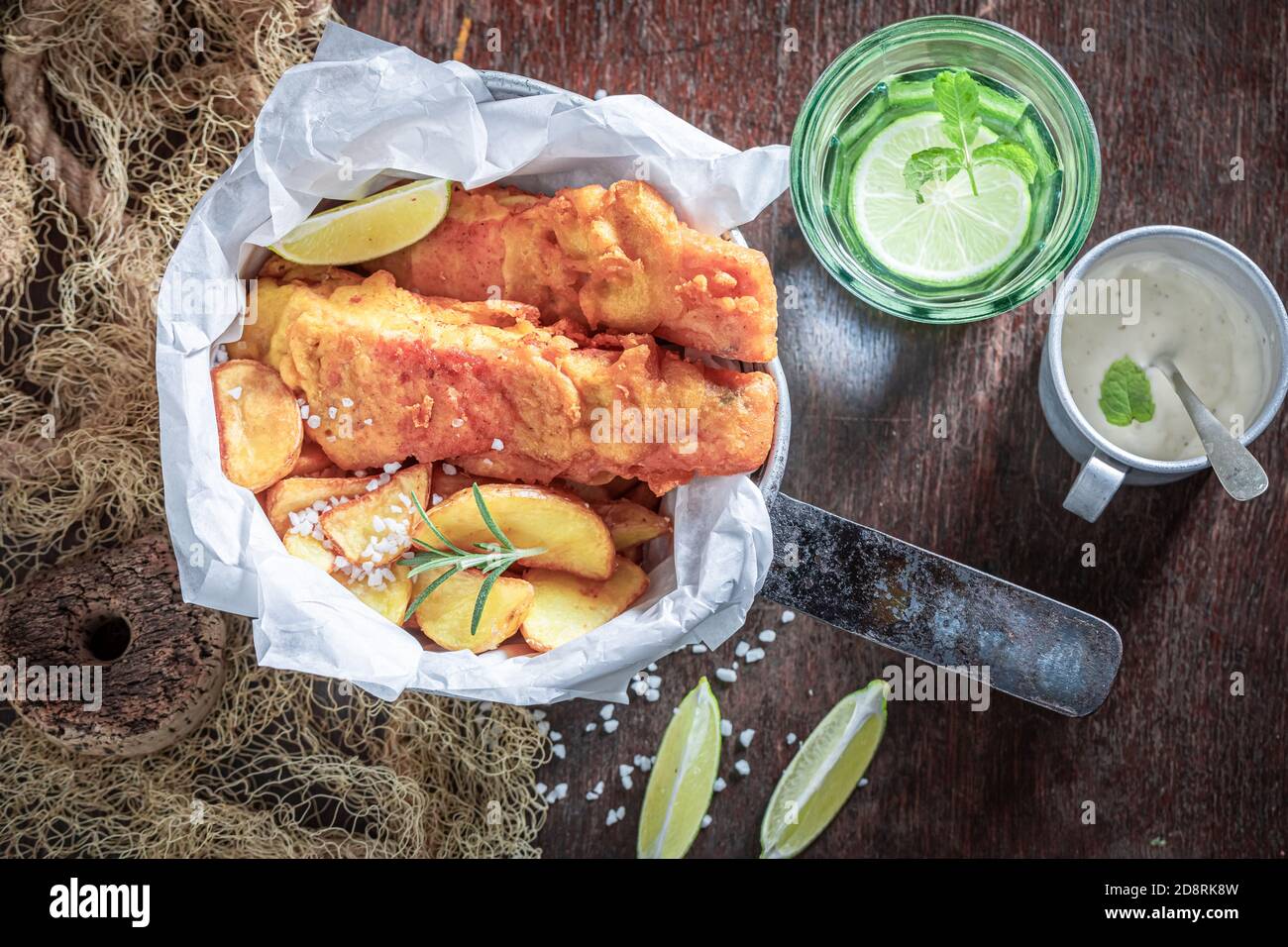 Pesce e patatine fatte in casa serviti con salse e lime on tavolo di legno Foto Stock