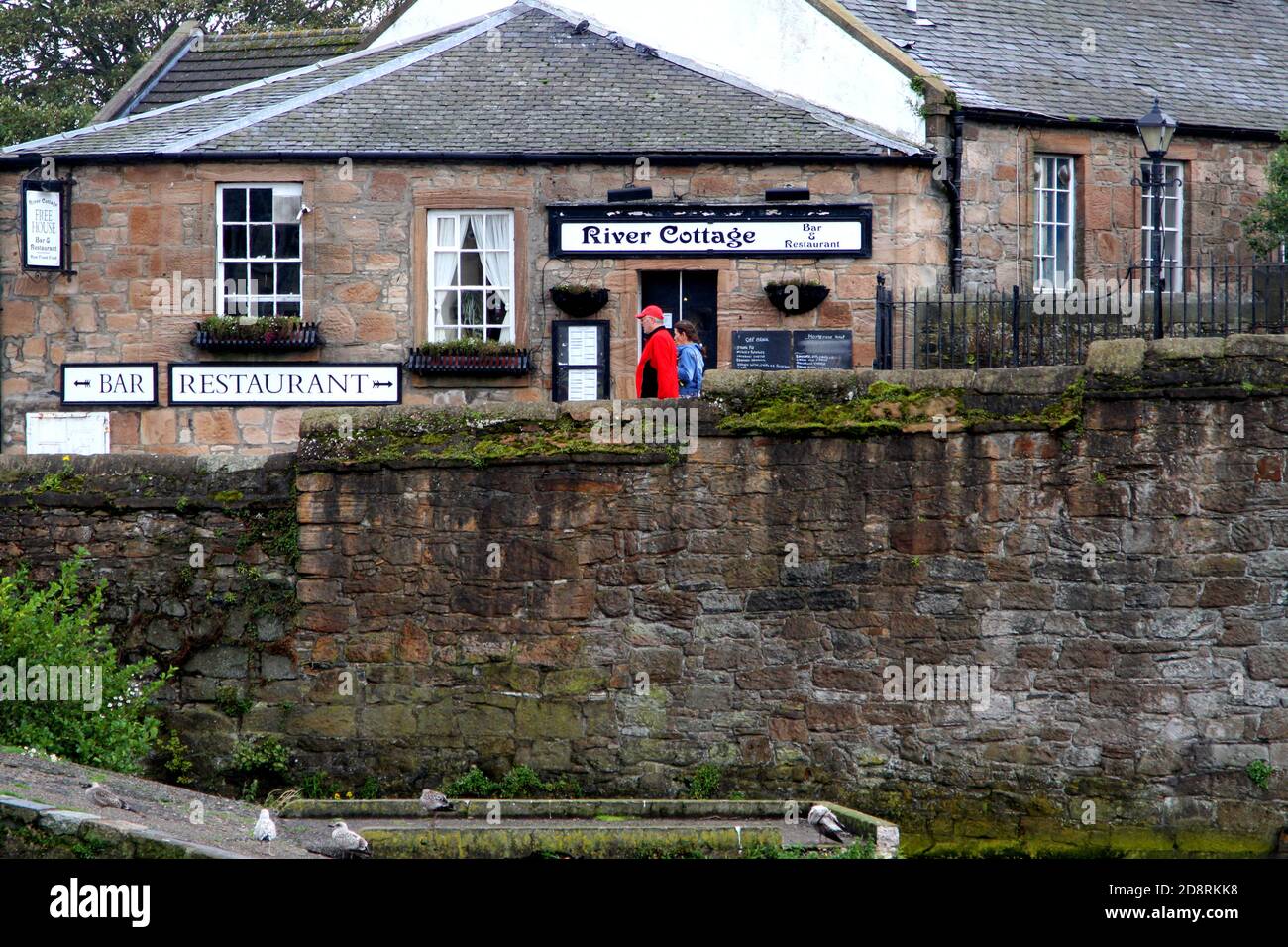 Ayr, Ayrshire, Scozia, Regno Unito. Fotografia di strada candida intorno ad Ayr. Coppia sul ponte passa un caffè chiamato River Cottage Foto Stock