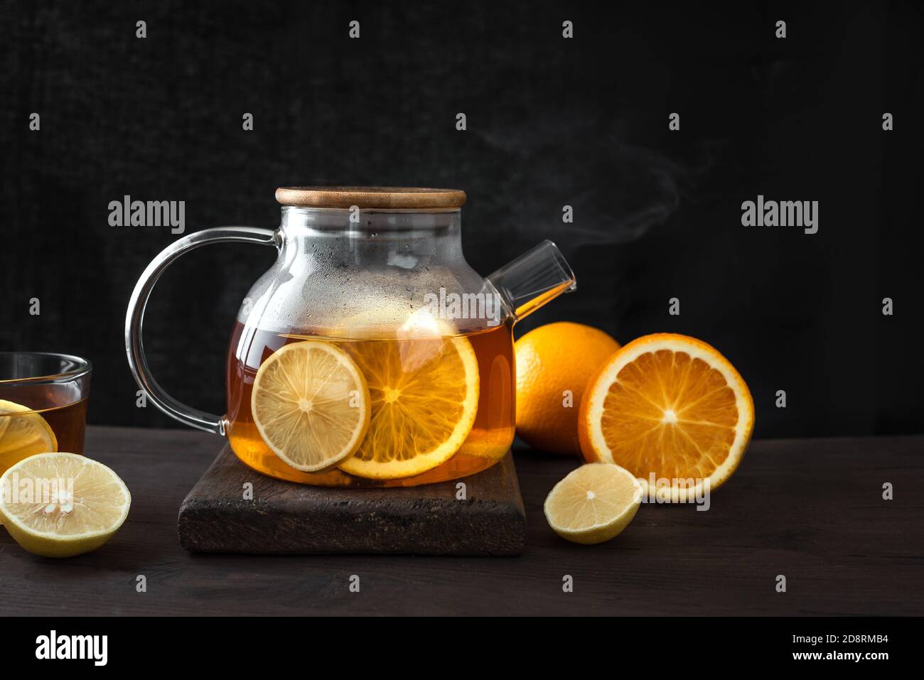 Tè agli agrumi con limone, arance in teiera trasparente su tavolo di legno scuro, spazio copia. Tè alla frutta. Bevanda calda invernale d'autunno stagionale. Foto Stock
