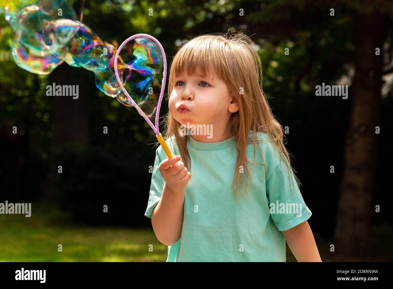 Bambino piccolo, ragazza che soffia bolle enormi da sola, ritratto all'aperto. Bambino giovane con guance soffiato soffia grandi bolle fuori, colpo closeup, ragazza attiva Foto Stock