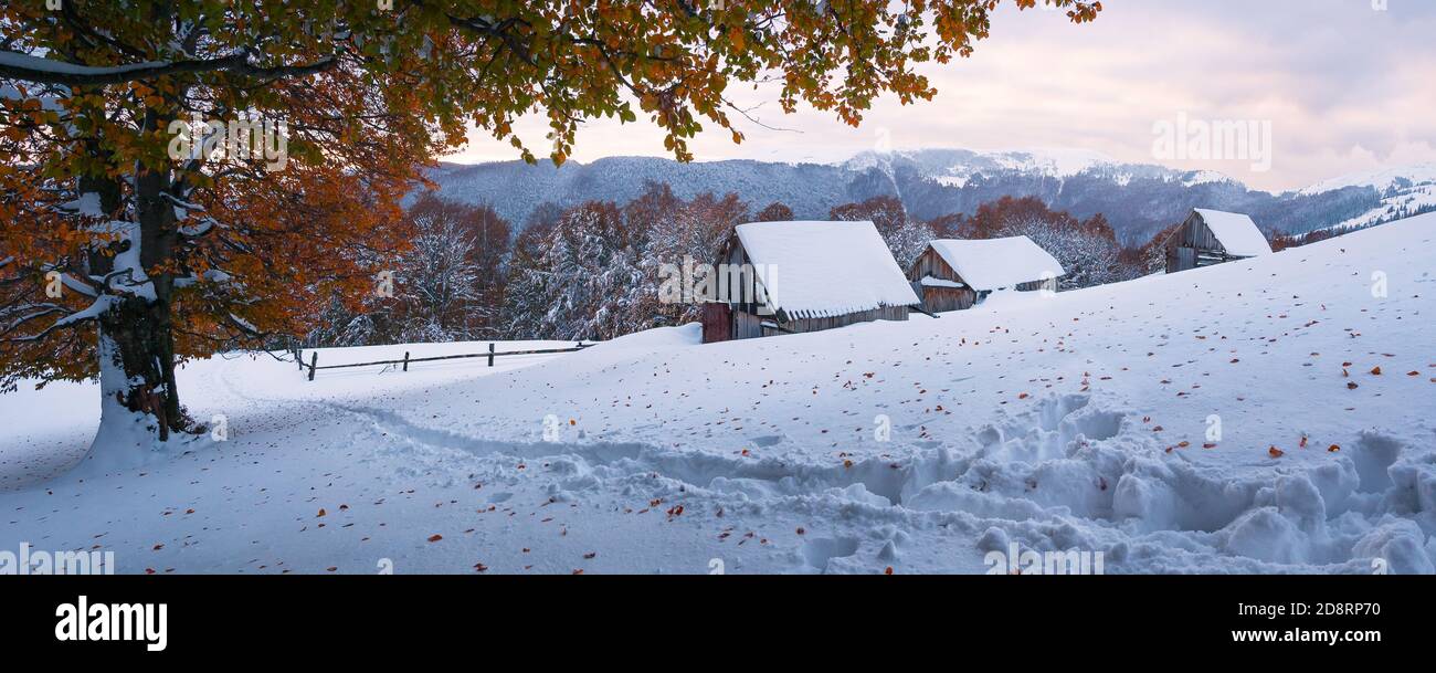 Paesaggio autunnale con la prima neve inaspettata. Vecchie capanne di pastori in legno su una collina di montagna. Sentiero innevato Foto Stock