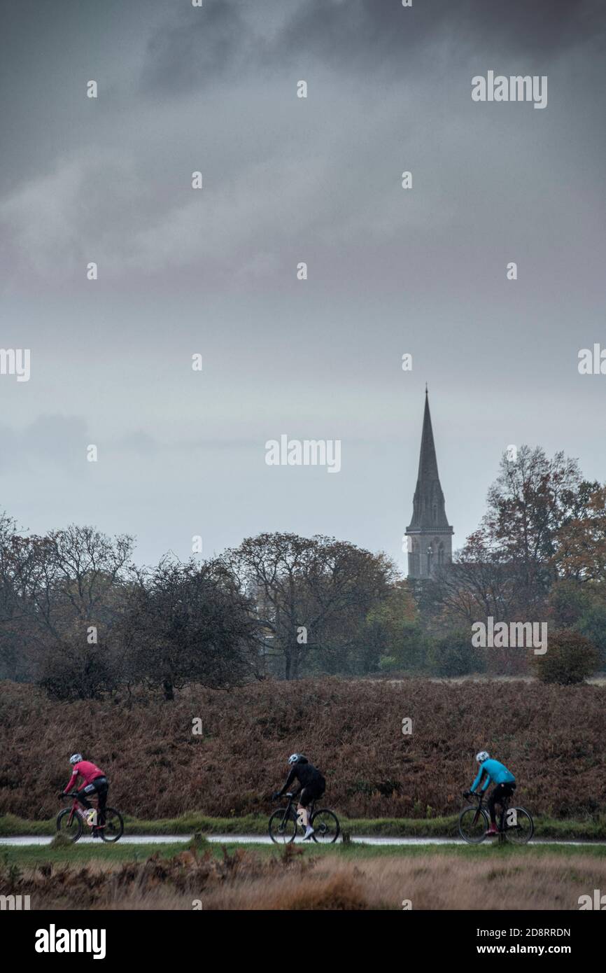 I ciclisti attraversano Richmond Park con la guglia di St Chiesa di Mattia in lontananza Foto Stock