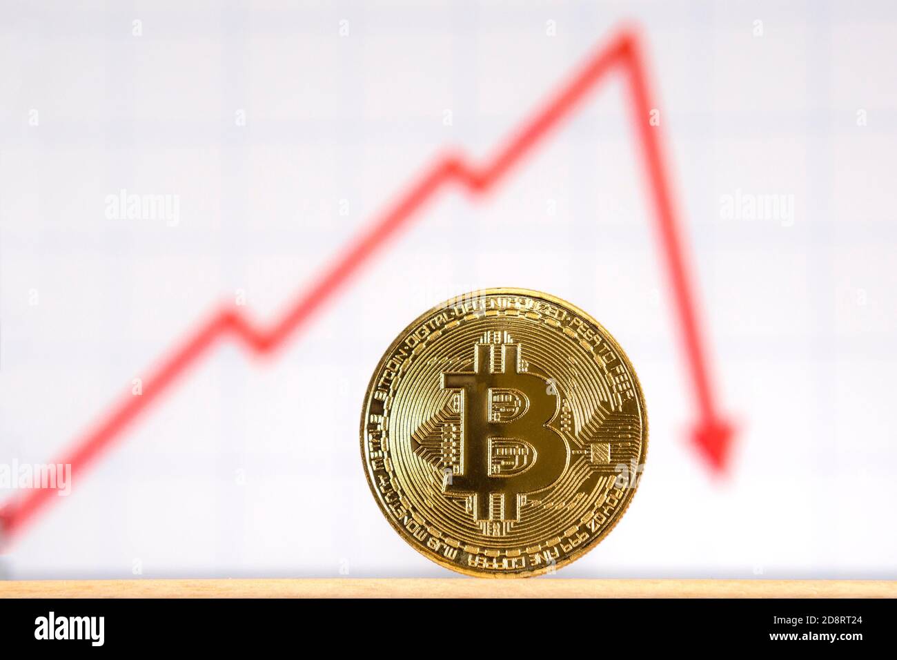 Una moneta d'oro davanti a un grafico rosso. Il grafico si alza e poi scende bruscamente, indicando una diminuzione del valore. Il grafico si trova al di fuori della profondità superficiale o Foto Stock
