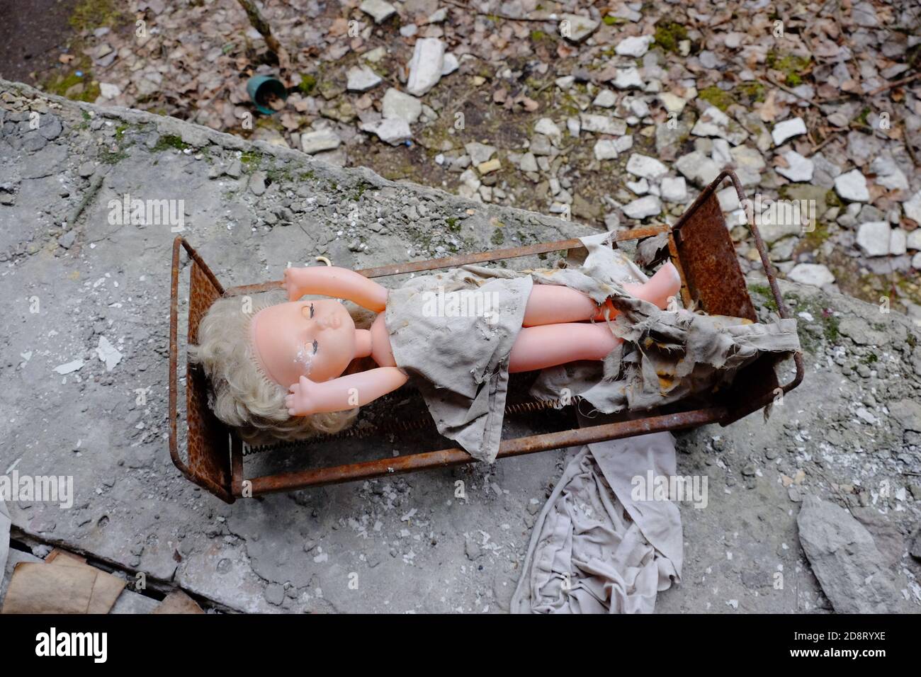 Bambola creepy su un lettino giocattolo. Giocattoli abbandonati in un asilo nido a Pripyat. Foto Stock Bambola creepy su un lettino giocattolo. Giocattoli abbandonati in un asilo nido a Pripyat. Foto Stock