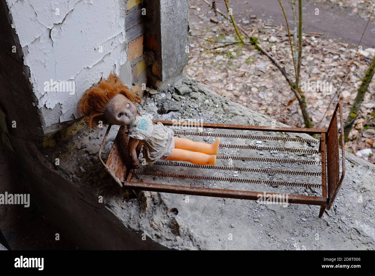 Bambola creepy su un lettino giocattolo. Giocattoli abbandonati in un asilo nido a Pripyat. Foto Stock Bambola creepy su un lettino giocattolo. Giocattoli abbandonati in un asilo nido a Pripyat. Foto Stock