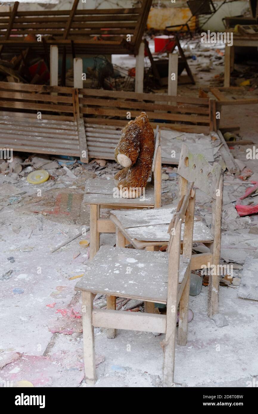 Giocattolo peluche sporco sulla sedia. Un orsacchiotto senza testa in un asilo abbandonato a Pipyat. Foto Stock