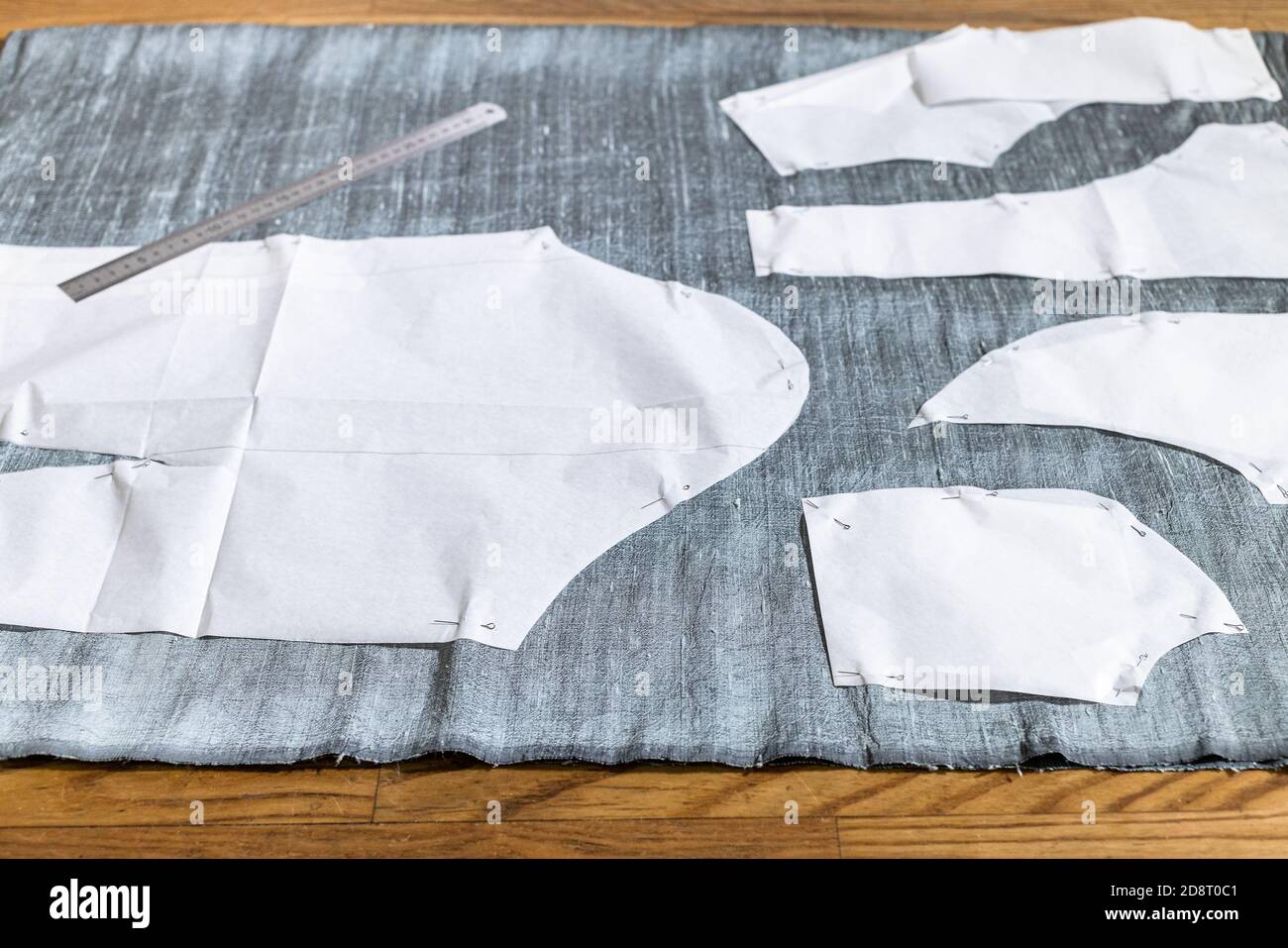 layout del modello di cucitura della carta di abito e righello in acciaio su tessuto grigio su tavolo di legno a casa Foto Stock