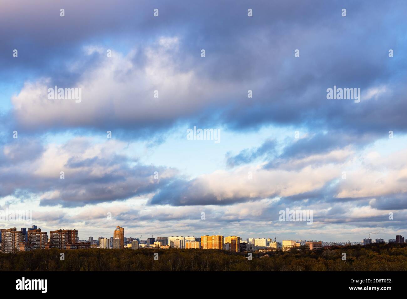 basse nuvole grigie nel cielo blu sulla città illuminata da tramonto sole al crepuscolo d'autunno Foto Stock