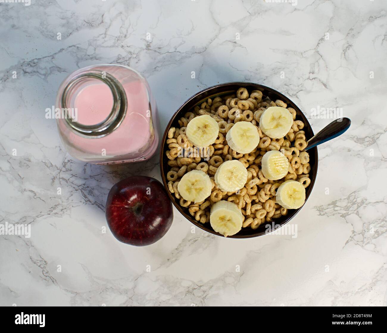 Guardando verso il basso la ciotola di cereali con fette di banana, mela rossa e latte rosa Foto Stock