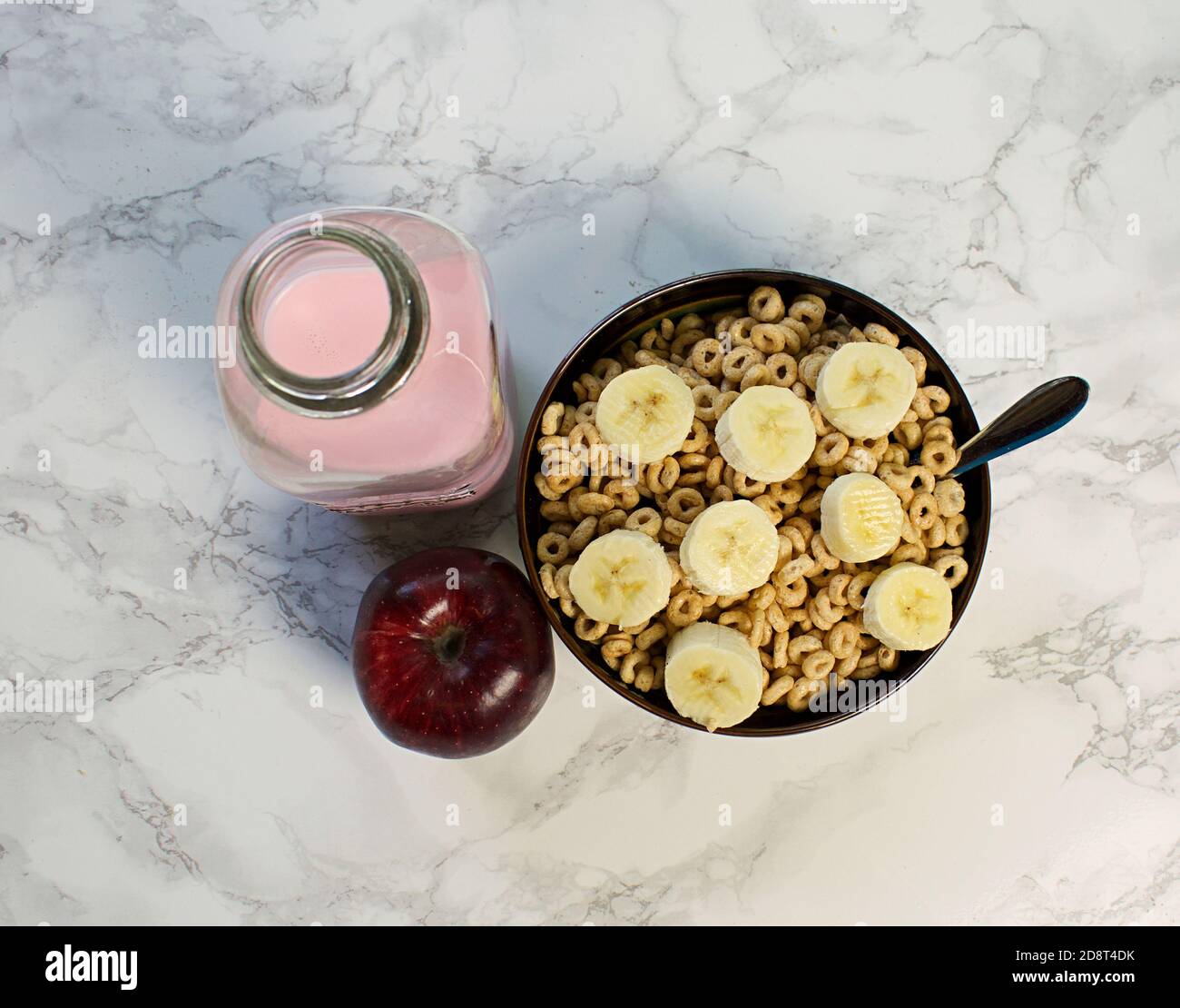Guardando verso il basso la ciotola di cereali con fette di banana, mela rossa e latte rosa Foto Stock
