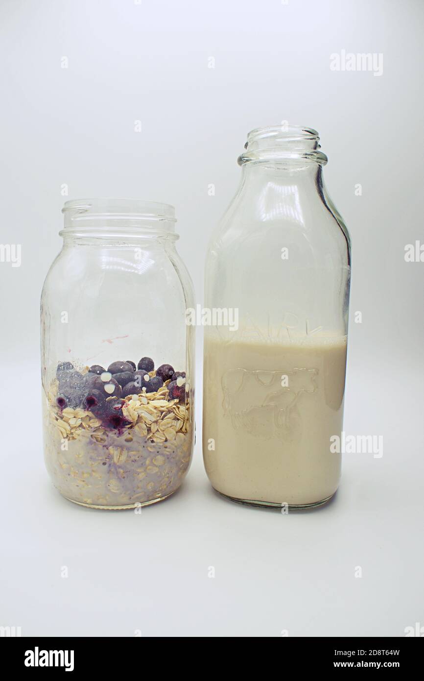 Vasetto con colazione di avena e mirtilli e latte d'avena versato in un vaso di vetro di mason. Foto Stock