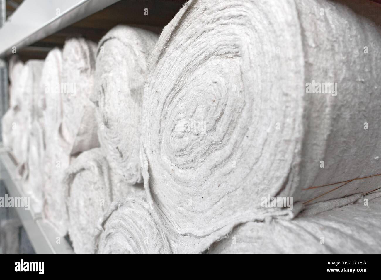 Il materiale bianco in rotoli si trova sui ripiani del magazzino. Materiale di copertura. Tessili per la produzione di stracci. Foto Stock