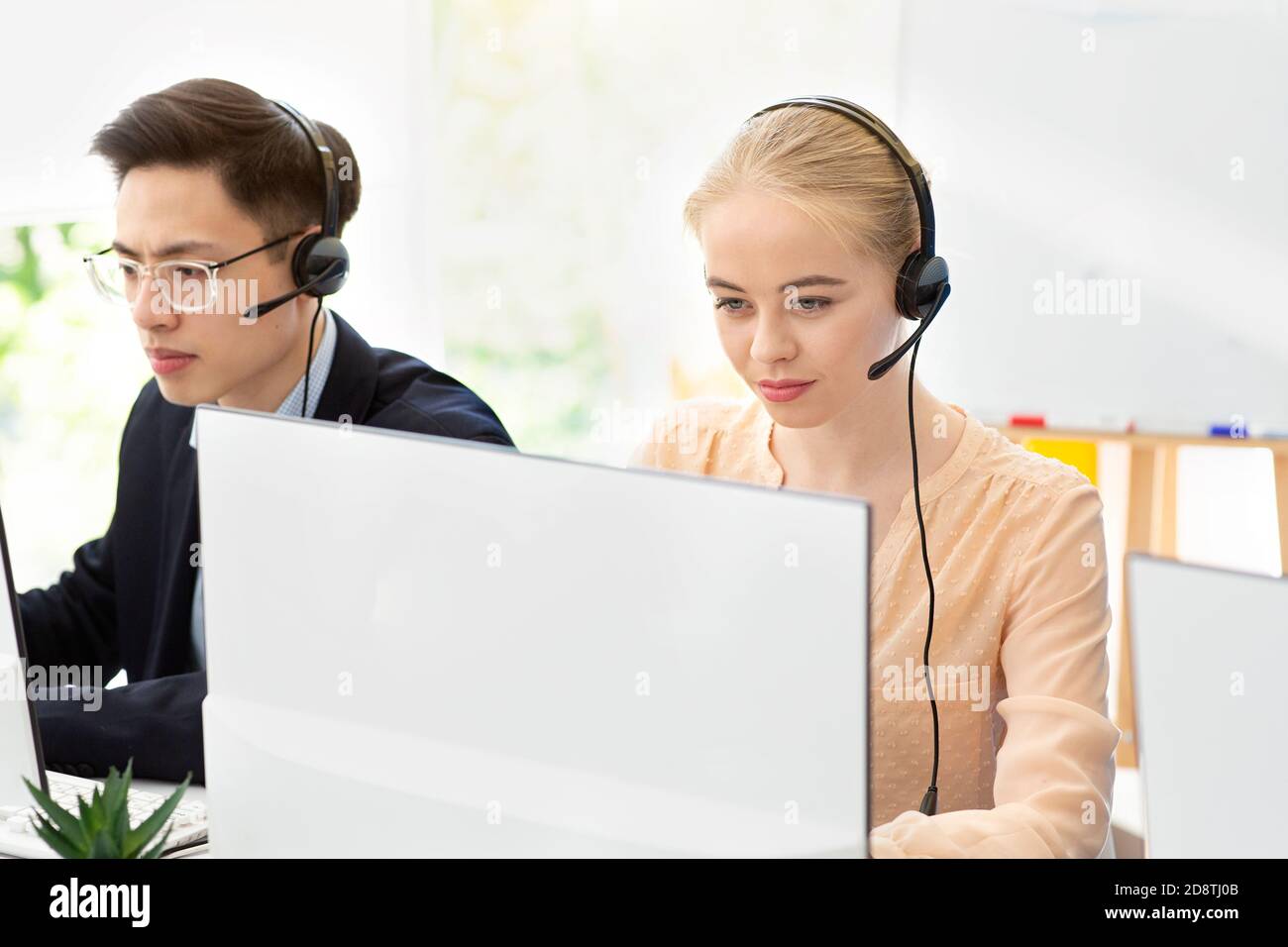 Giovani operatori di supporto tecnologico al lavoro in un call center contemporaneo Foto Stock