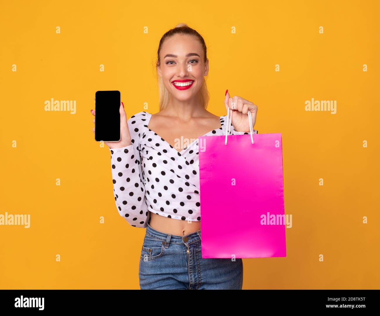 Donna sorridente che mostra lo schermo nero del telefono e la borsa della spesa Foto Stock