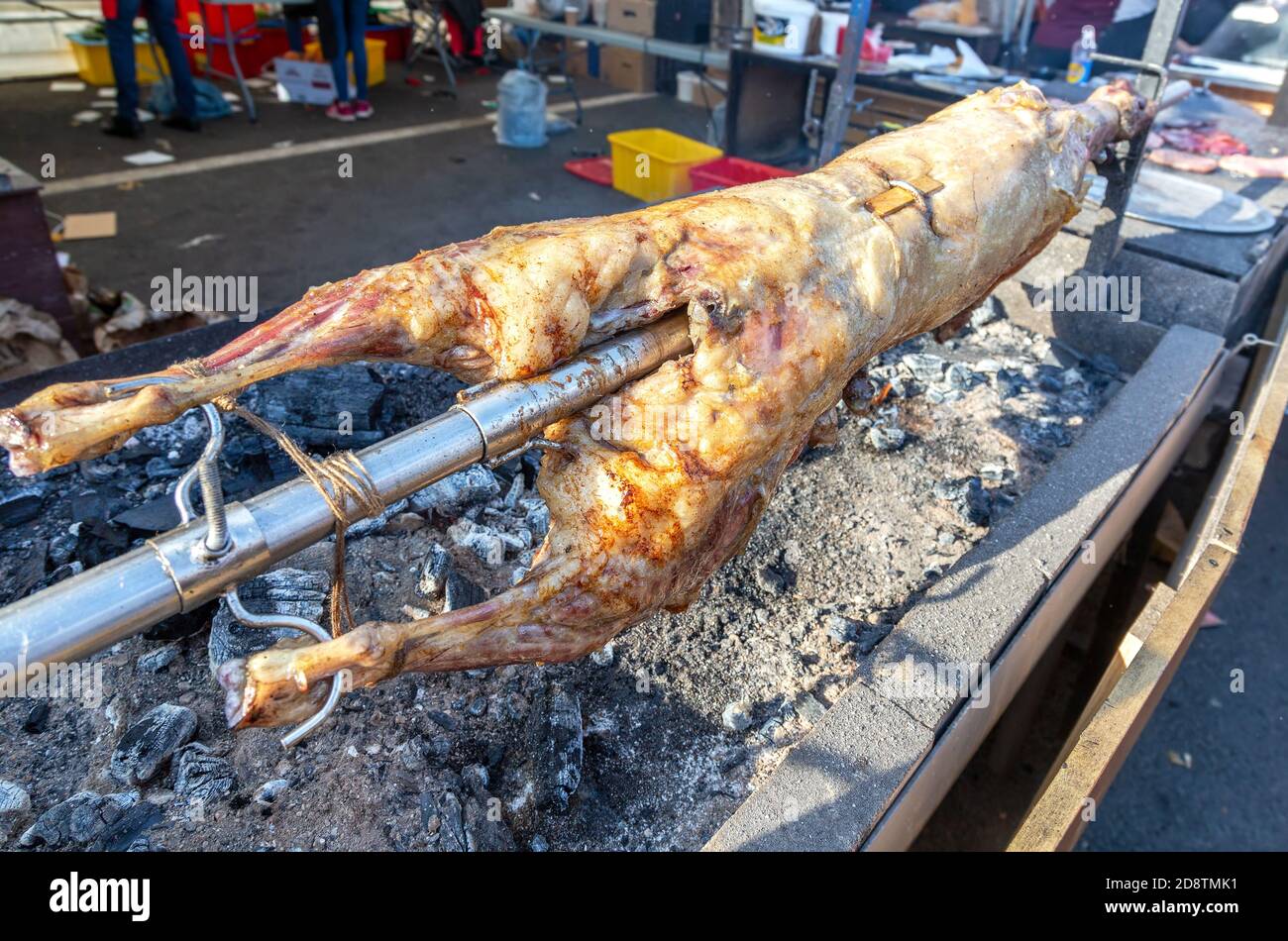 Cottura carcasse di agnello su uno spiedo arrostito sul fuoco aperto della griglia barbecue nel mercato di strada. Tradizionale arrosto di agnello serbo o o barbecue di maiale Foto Stock