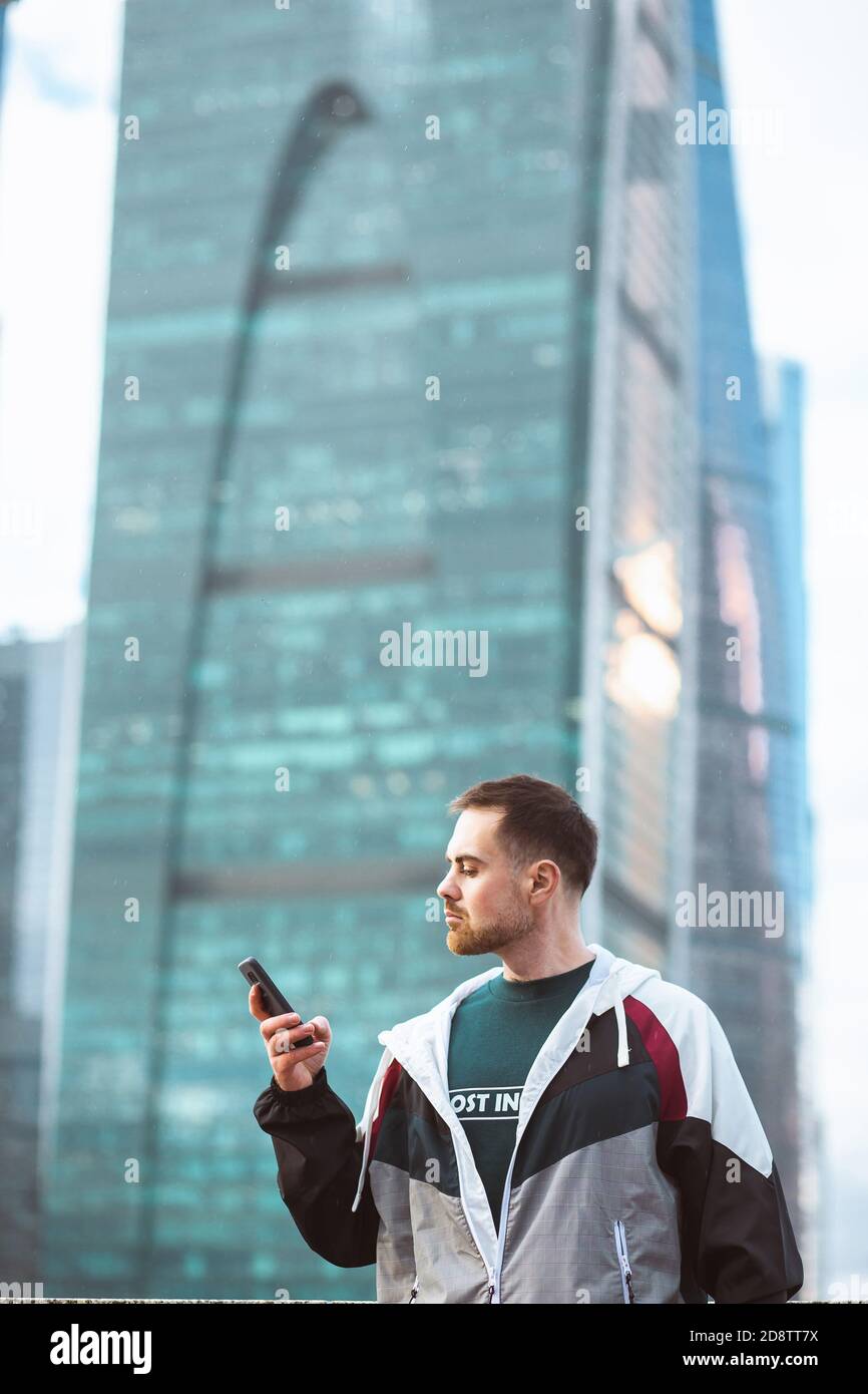 Bell'uomo casual in posizione di frangivento con smartphone su una vista grattacielo. Foto Stock