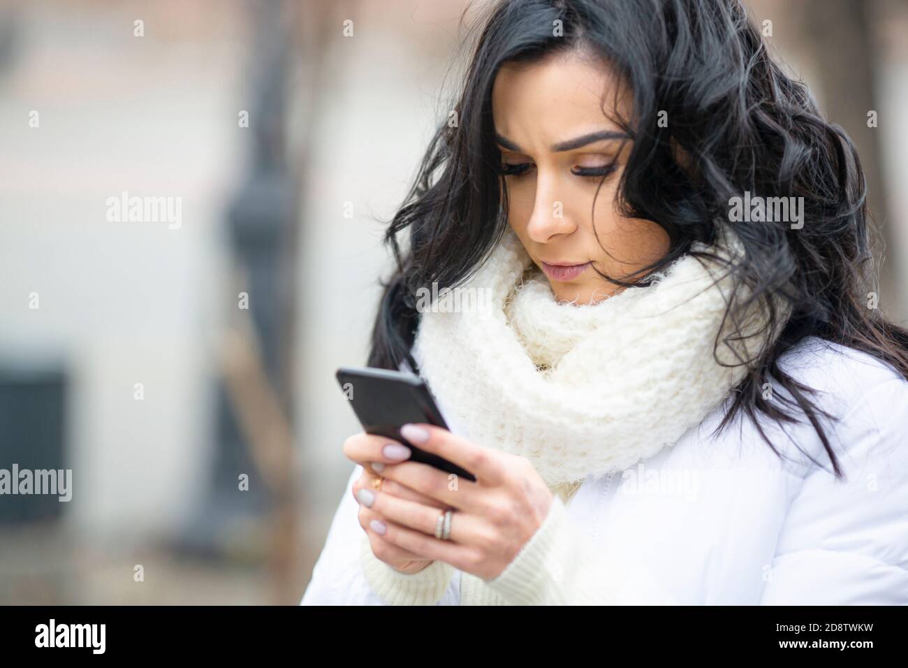 Primo piano della foto di una brunetta b eautiful con un Smartphone sulla strada di una città europea nel stagione invernale Foto Stock