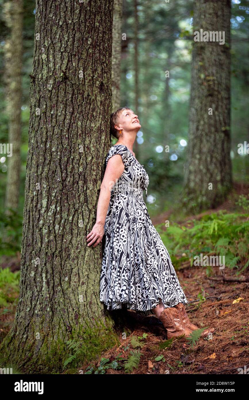 Gioiosa donna appoggiata contro l'albero nella foresta guardando in su nella meraviglia - Brevard, Carolina del Nord, Stati Uniti Foto Stock