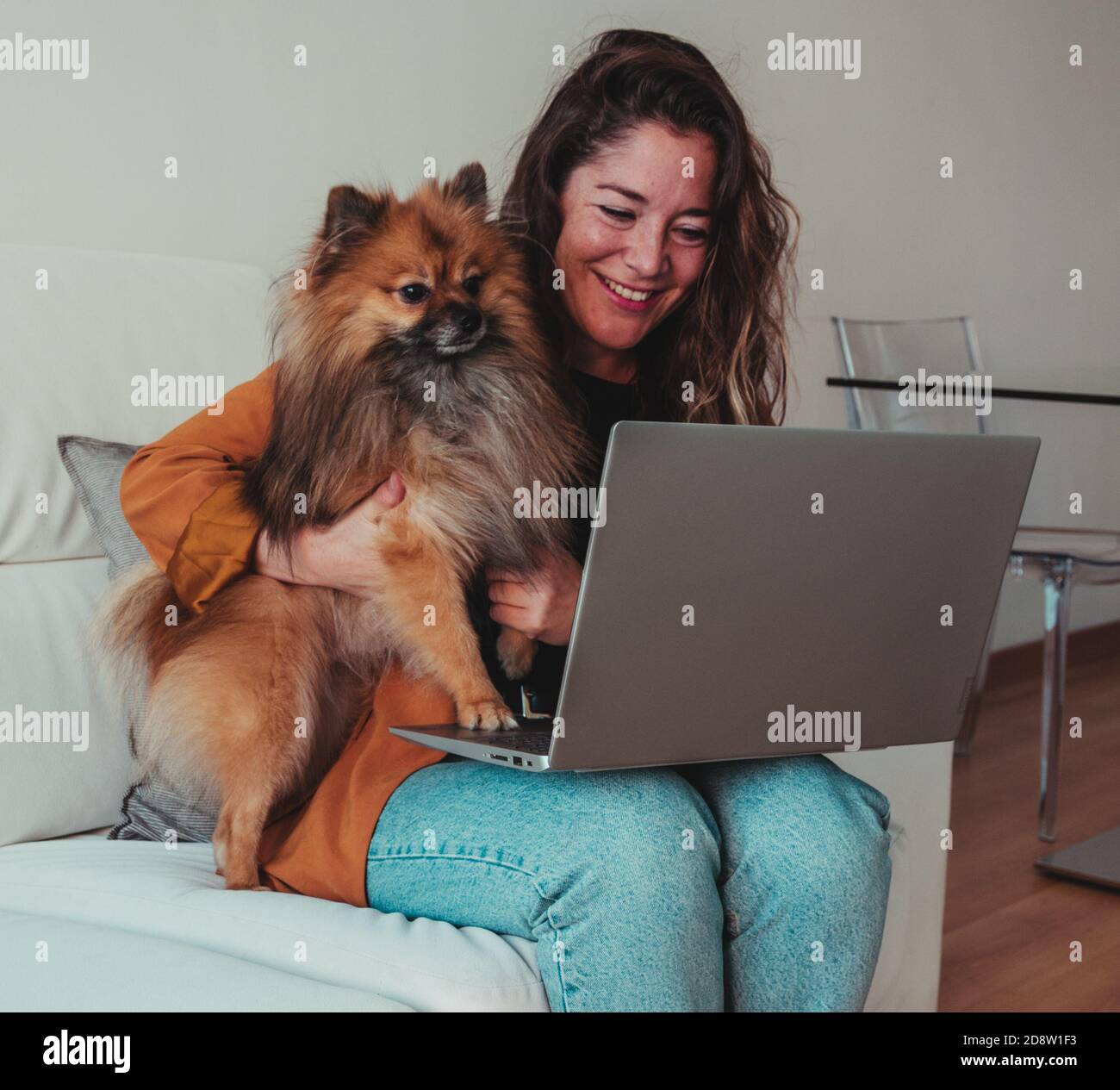 Donna felice che accarezzava il suo cane sul divano mentre fanno una videochiamata. Tempo piacevole e felice. Foto Stock