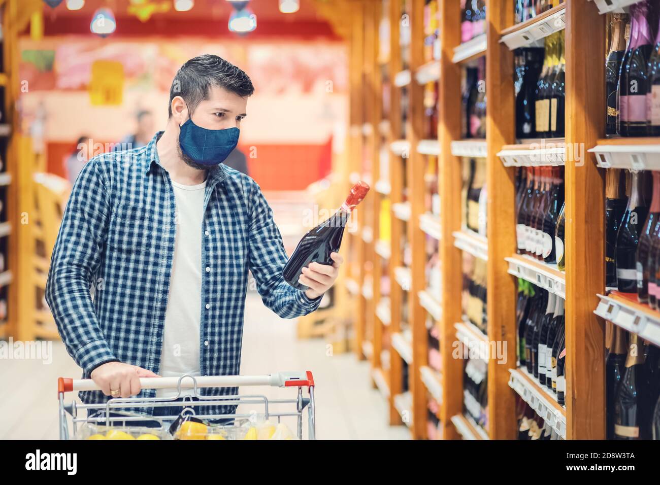 Giovane uomo con maschera protettiva shopping vino rosso da supermercato durante la riapertura del coronavirus focolaio Foto Stock