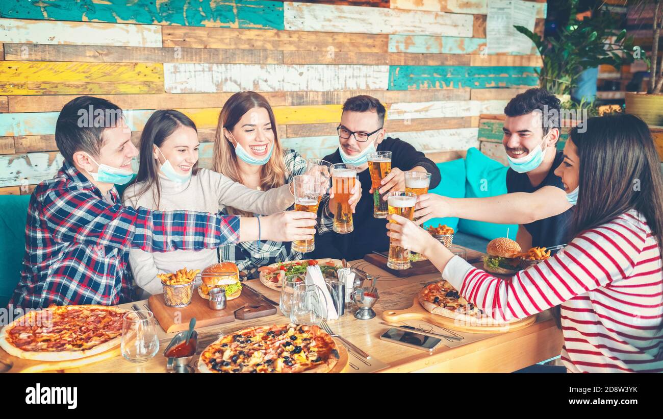Felici i giovani amici con maschere protettive che mangiano e bevono birra al ristorante Foto Stock