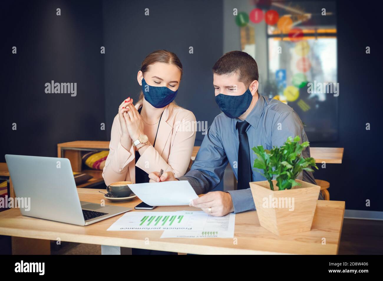 Uomini d'affari con maschere che lavorano insieme su laptop in moderno ufficio di codorking Foto Stock