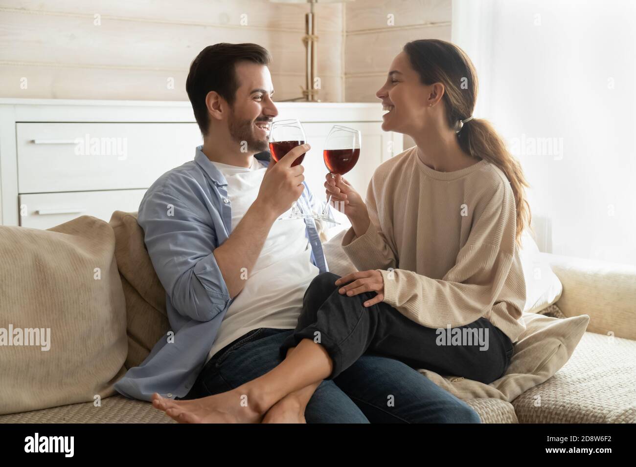 Famiglia millenaria seduta sul divano con bicchieri da vino per festeggiare l'anniversario Foto Stock