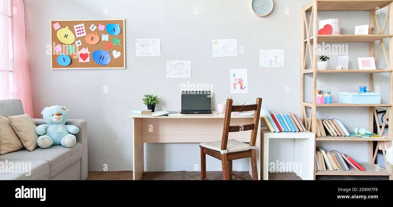 Spazio interno per bambini con tavolo, divano, libri e computer portatile sul tavolo a casa. Foto Stock