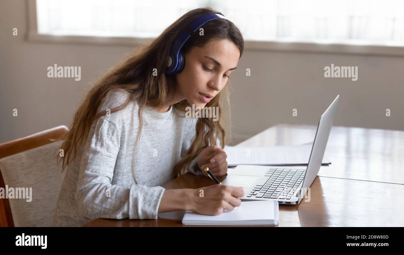 Studentessa seduta da computer portatile in auricolari che ascoltano lezioni lontane Foto Stock