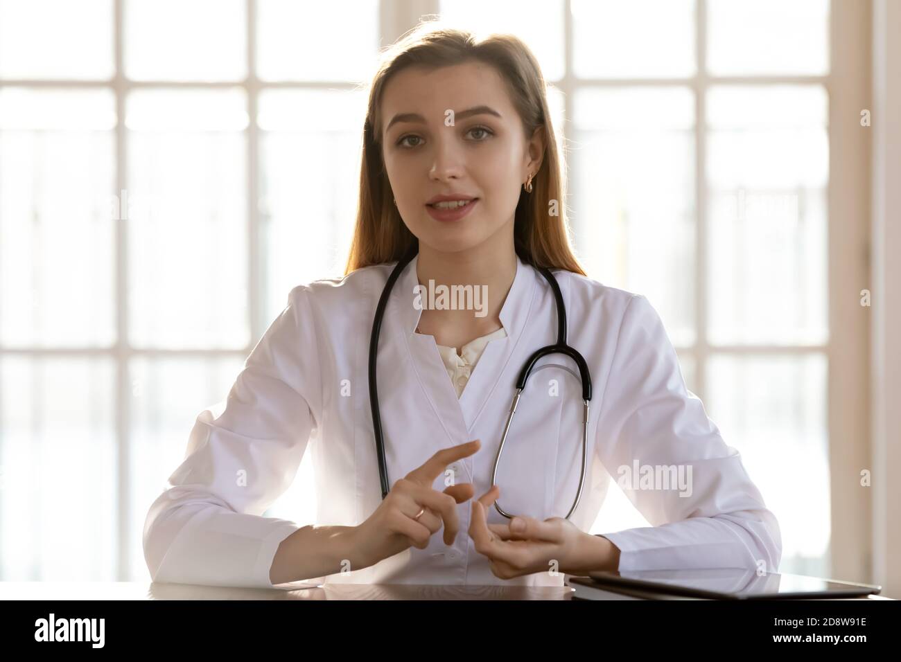 Sicuro medico femminile seduta alla scrivania che consulta paziente online Foto Stock