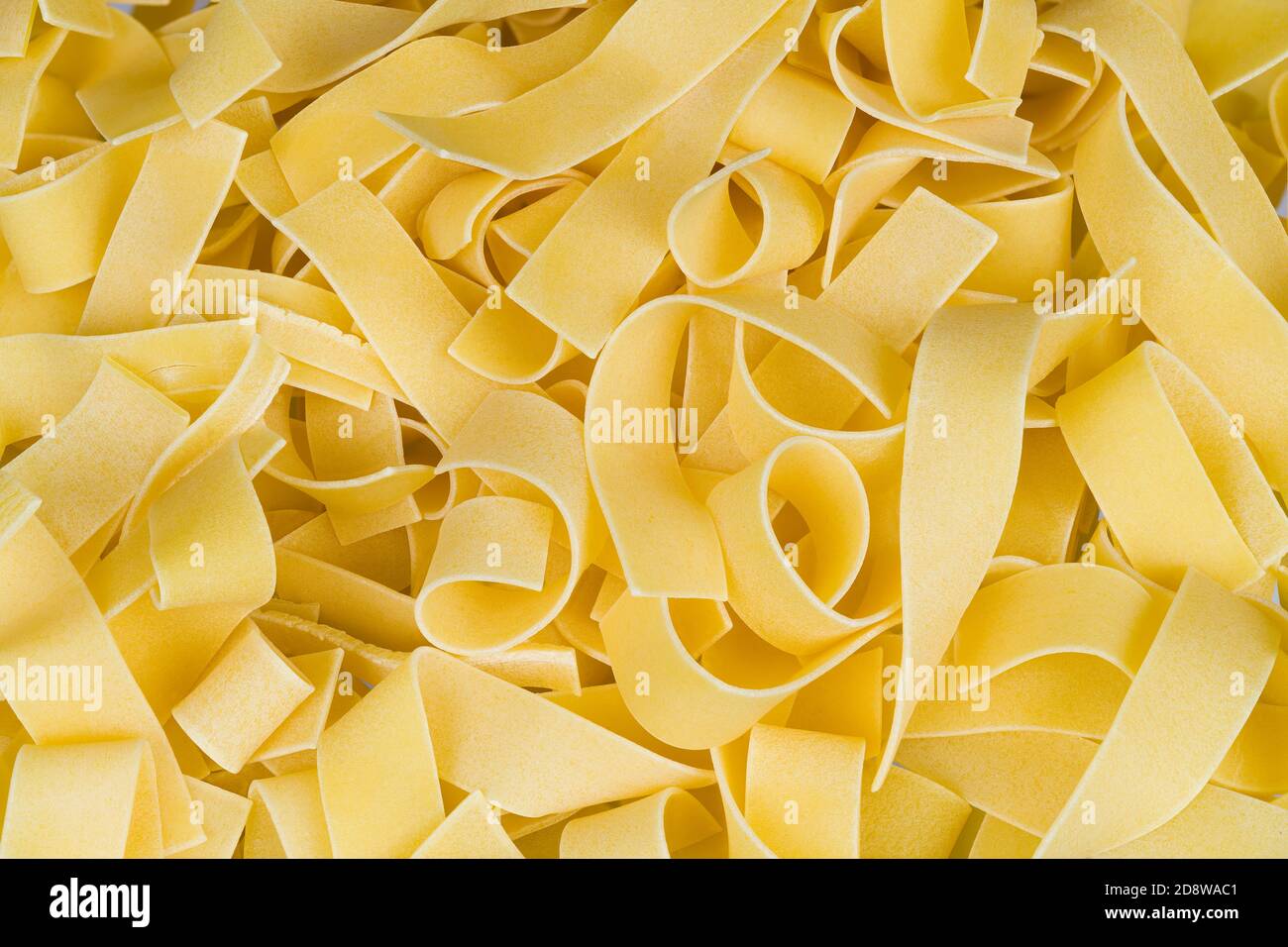 Pasta all'uovo gialla con tagliatelle larghe e ondulate. Tagliatelle a nastro piatto e crudo arrotolate di pasta di grano in uno splendido sfondo di cucina italiana o asiatica. Foto Stock