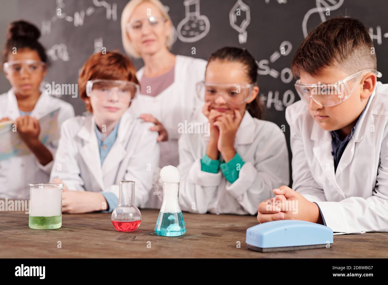 Schoolkids in biancetti e occhiali protettivi che osservano le reazioni chimiche Foto Stock