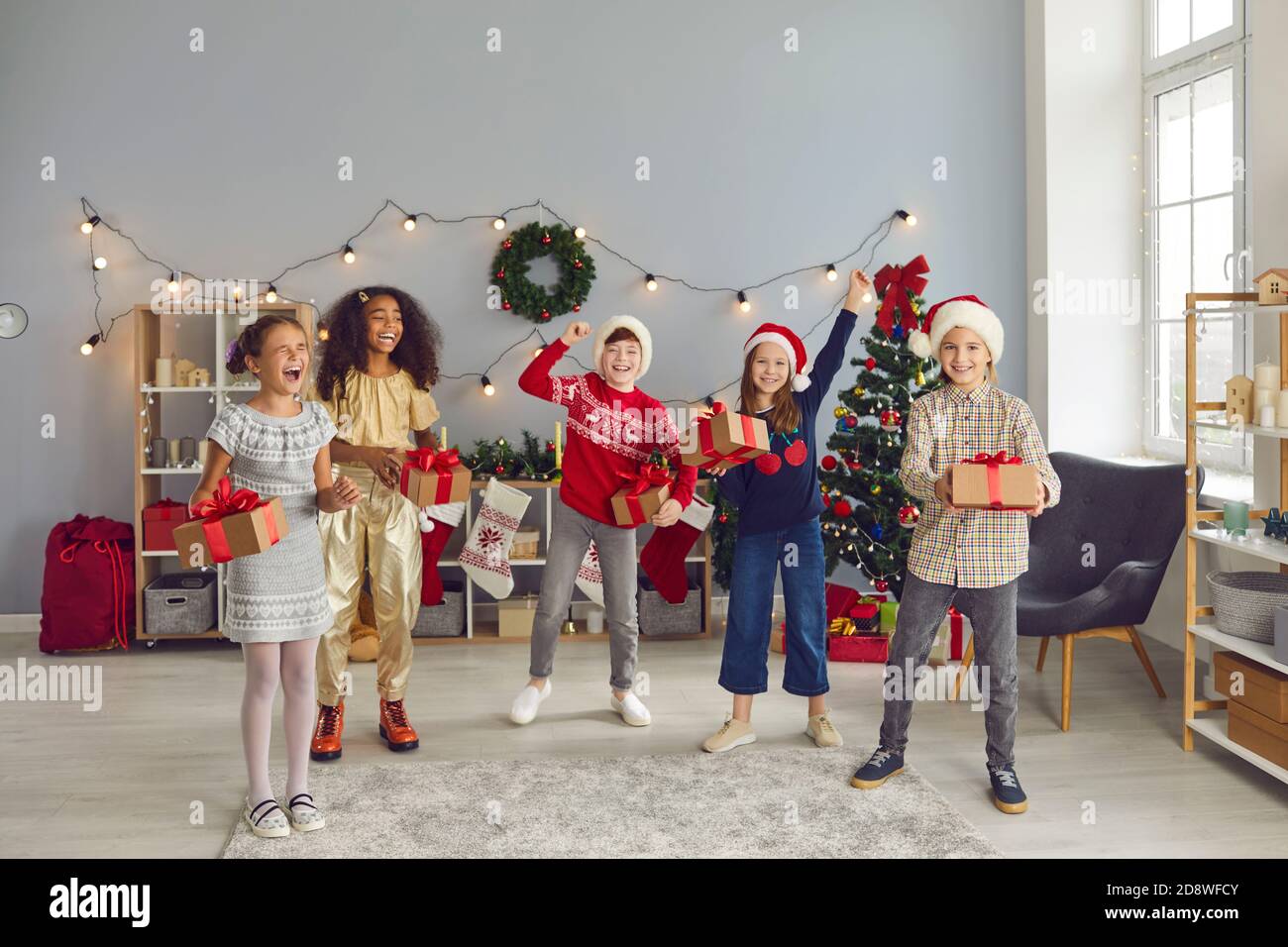 Gli amici dei bambini di razza mista saltano insieme, tenendo i regali e gioendo che Natale è venuto. Foto Stock