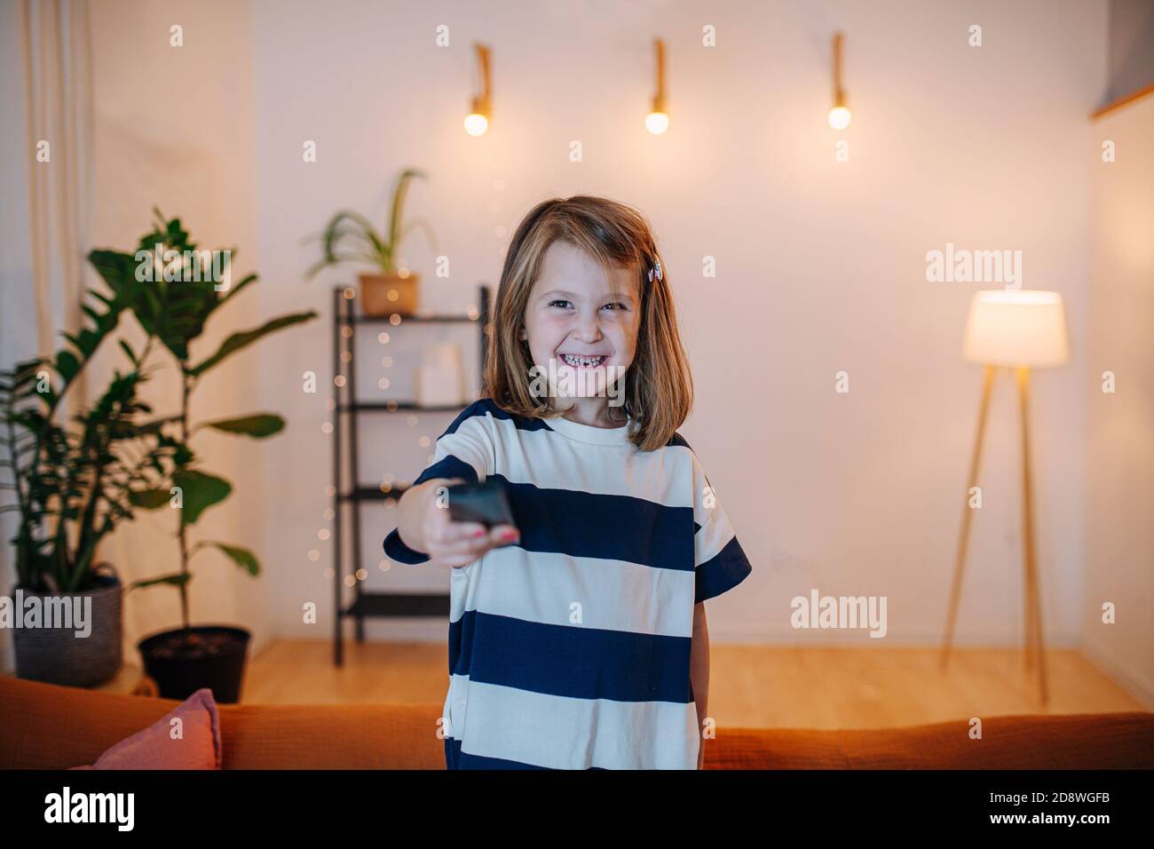 Allegra bambina che cambia canale TV con un telecomando Foto Stock