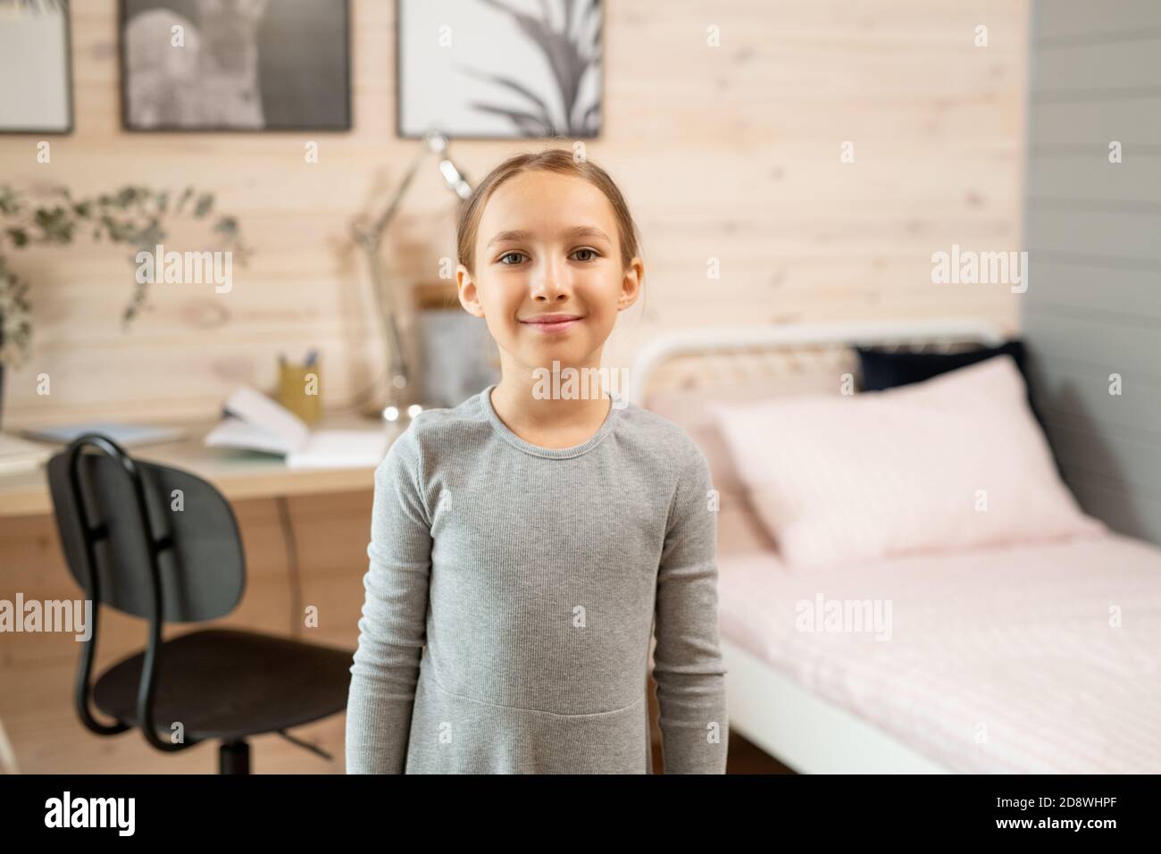 Studentessa contemporanea in abito grigio davanti alla macchina fotografica contro la stanza Foto Stock