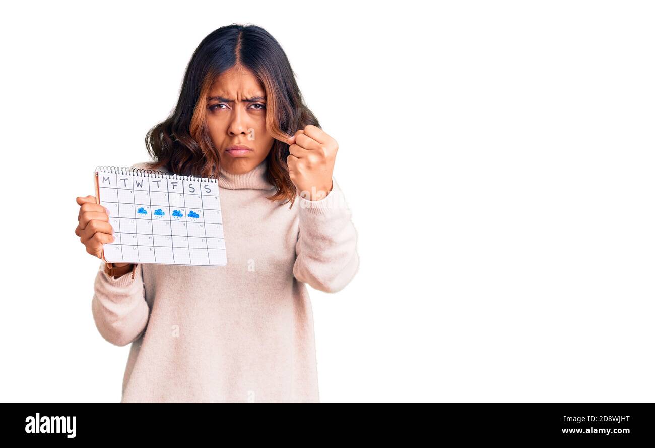 Giovane bella donna di corsa mista tenendo calendario di viaggio irritata e frustrata gridando con rabbia, urlando pazzo con rabbia e mano sollevata Foto Stock