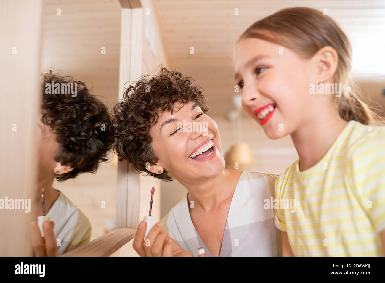 Bambina con rossetto sulle labbra guardando nello specchio mentre sua madre ridendo Foto Stock