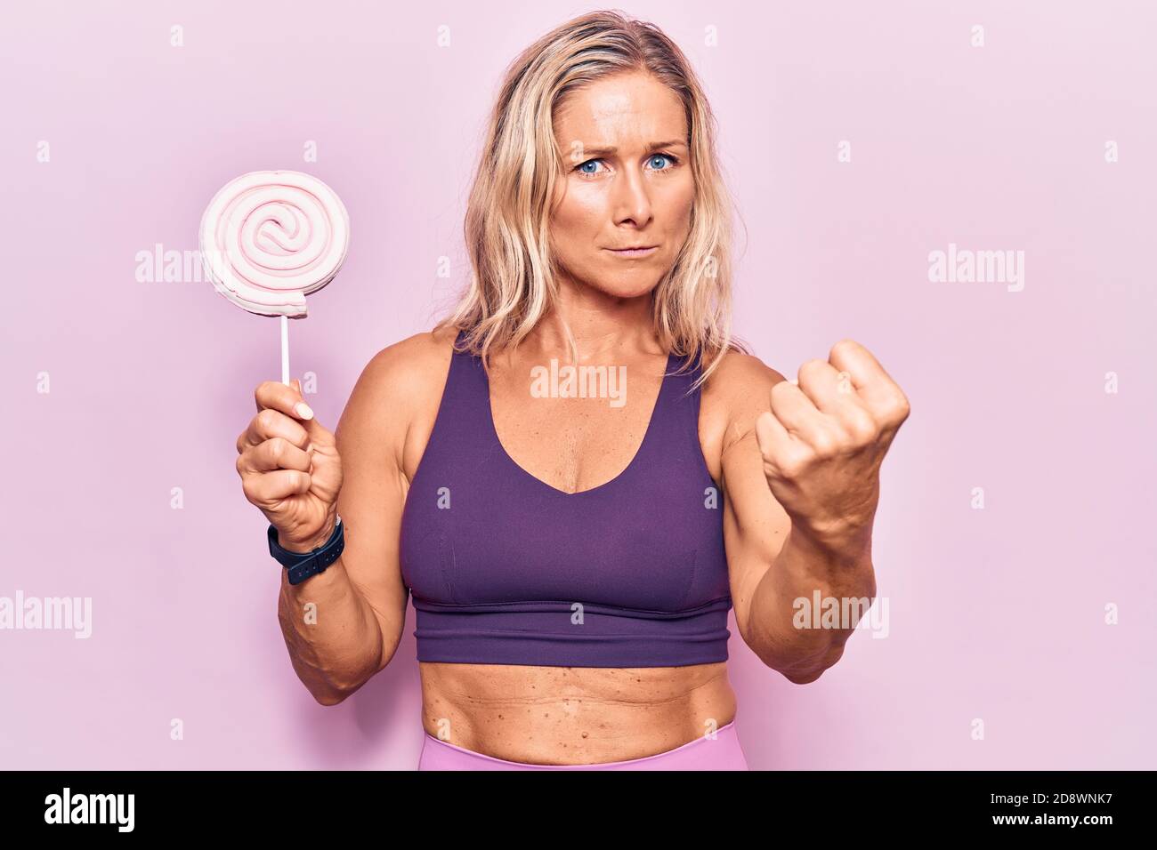 Donna bionda caucasica di mezza età che indossa abbigliamento sportivo che  tiene la caramella dello zucchero irritata e frustrata gridando con rabbia,  urlando pazzo con rabbia e mano Foto stock - Alamy