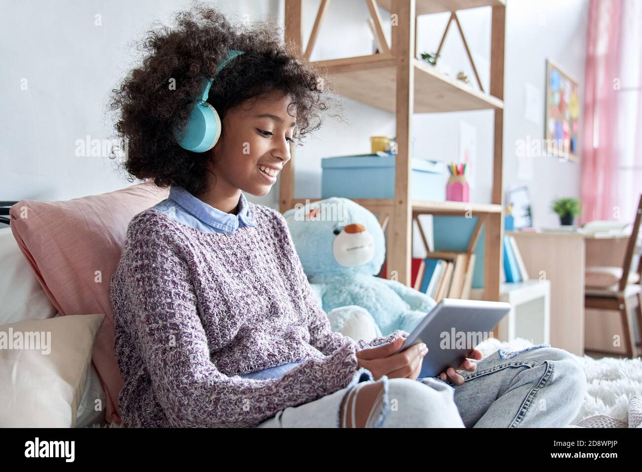Felice african american ragazza di capretto che tiene il elearning del tablet digitale seduto sul letto. Foto Stock