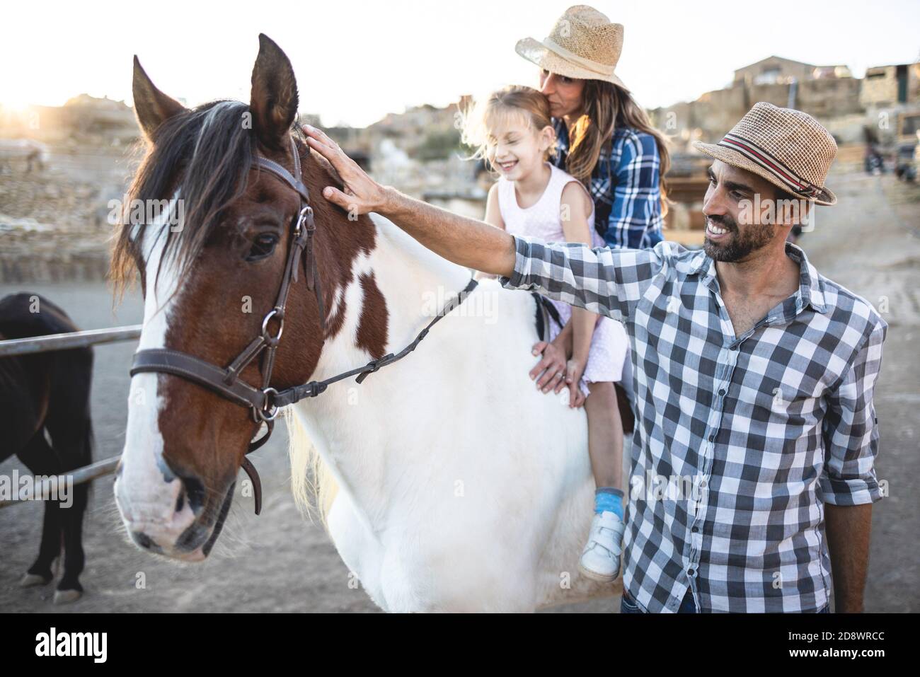 Felici i genitori con la figlia che cavalcano un cavallo al ranch della fattoria - stile di vita familiare e concetto di amore animale - Focus on faccia del padre Foto Stock