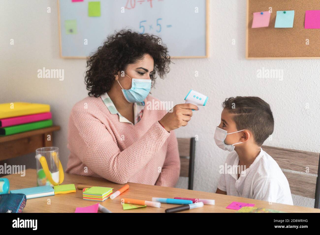 Insegnante che controlla la temperatura del bambino usando il termometro infrarosso a scuola - Mettere a fuoco sul volto della donna Foto Stock