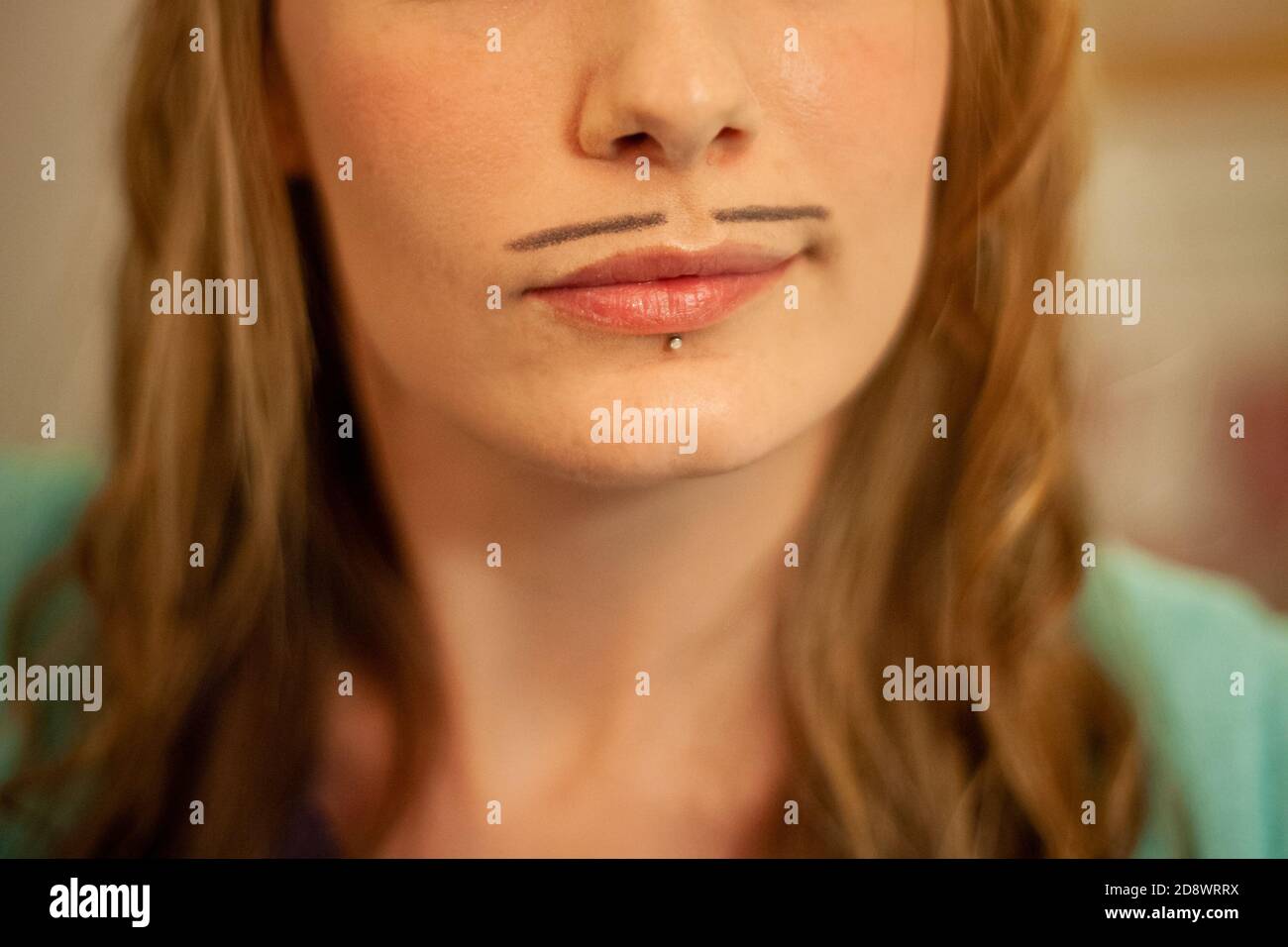 Primo piano della faccia inferiore della giovane donna, con una leggendaria caratteristica del viso disegnata: I baffi a matita, per Movember. Anche un piercing labbro. Foto Stock