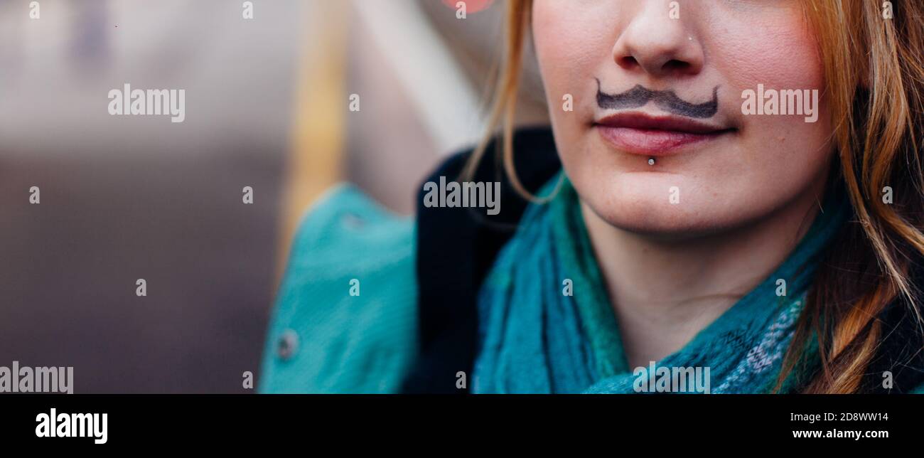 Primo piano del viso inferiore della giovane donna, con una caratteristica facciale disegnata; il corto e riccio, i baffi di poirot, con un labbro forato, per Movember. Foto Stock