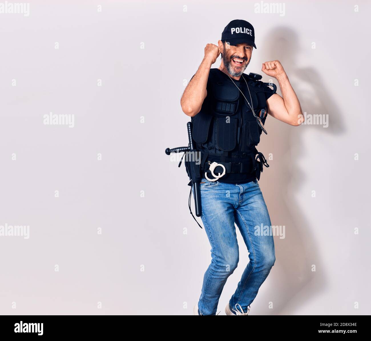 Bell'uomo di mezza età che indossa un'uniforme di polizia sorridente felice. Saltando con sorriso sul viso facendo segno ok con pugni su sfondo bianco isolato Foto Stock