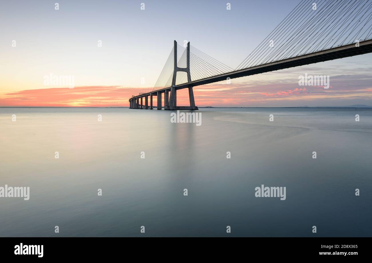 Sfondo con l'alba colorata sul ponte di Lisbona. Il ponte Vasco da Gama è un punto di riferimento e uno dei ponti più lunghi del mondo. lan urbana Foto Stock