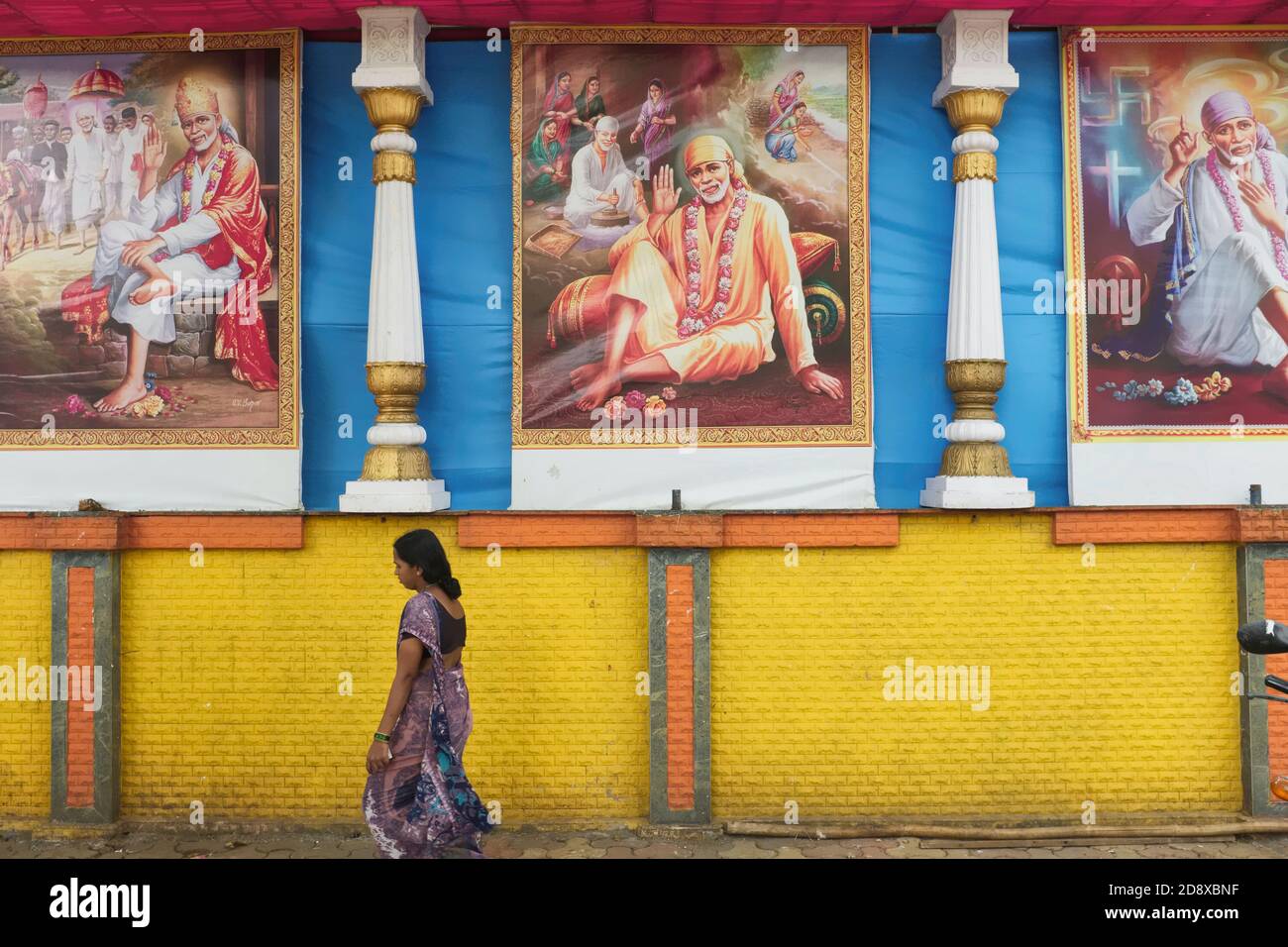 Una donna a Mumbai, India, che cammina sotto murali raffiguranti Shirdi Sai Baba, un venerato santo indù (?-1918), da non confondere con Satya Sai Baba Foto Stock