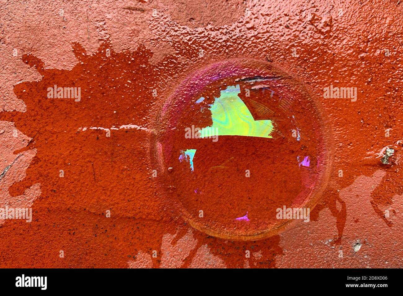 La vista dall'alto di una mezza bolla di sapone si trova su un mattone rosso incrinato. Acqua saponata con riflessi colorati Foto Stock