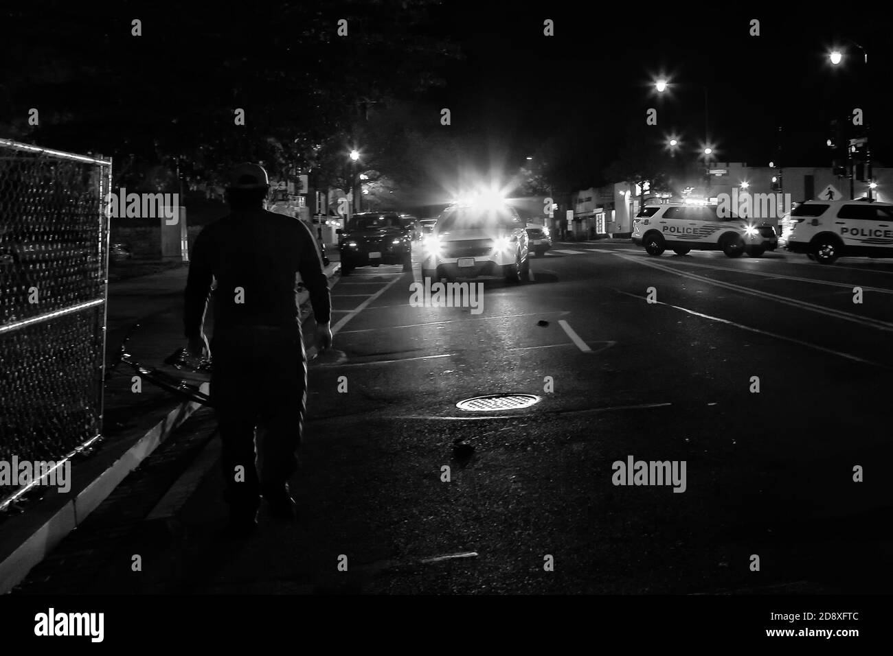 Un uomo cammina verso le auto della polizia con luci lampeggianti durante le proteste contro la polizia per la morte di Karon Hylton, Washington, DC, USA Foto Stock
