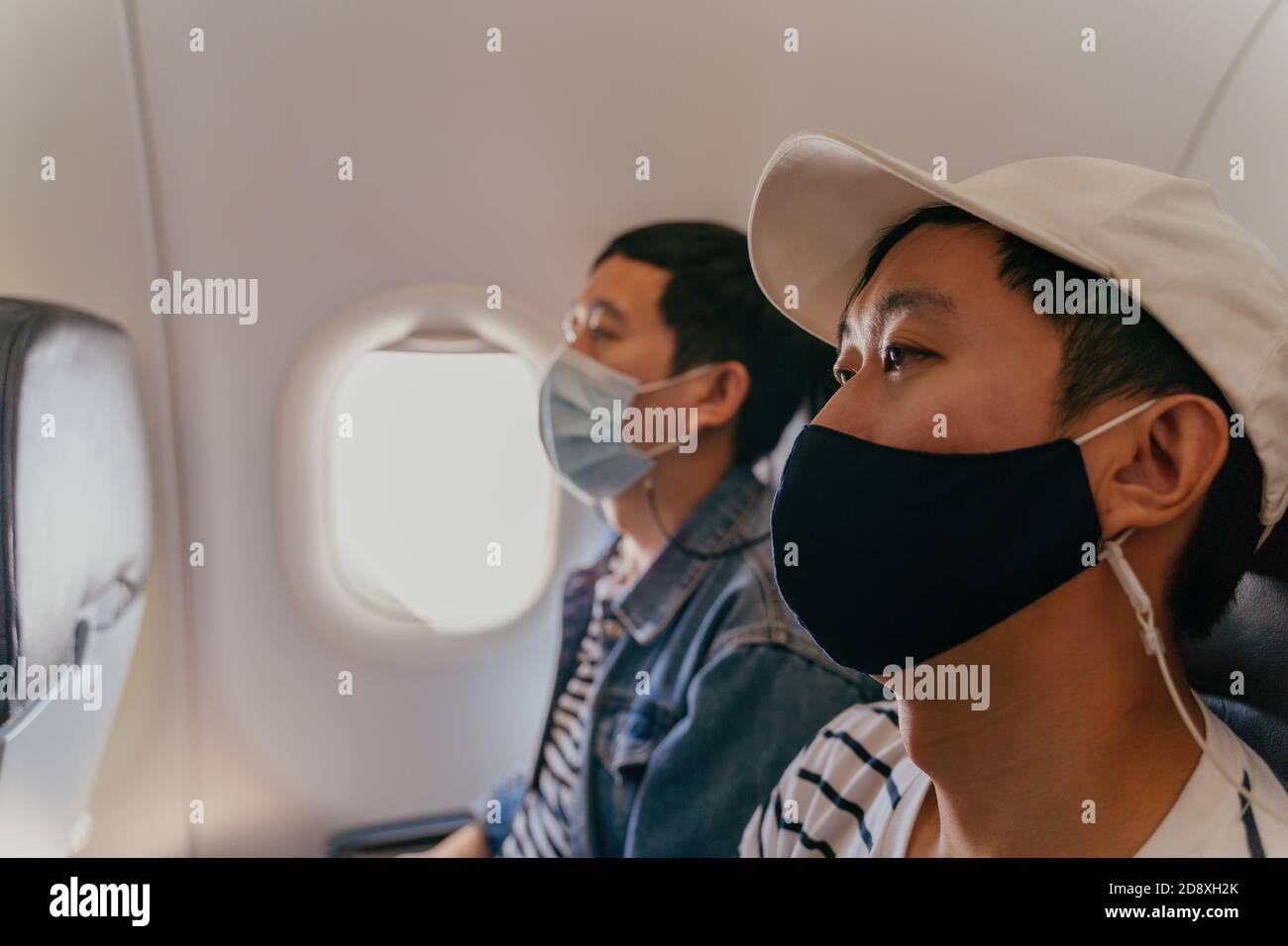 20s giovani adulti asiatici maschi turisti che indossano una maschera all'interno dell'aereo cabina aria. Trasporto pubblico durante Covid-19 o pandemia di Coronavirus. Nuovo concetto di viaggio normale. Foto Stock